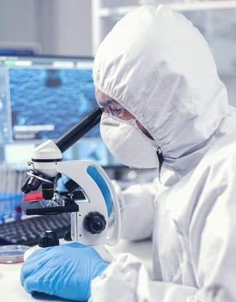 Researcher in a PPE suit working at a microscope
