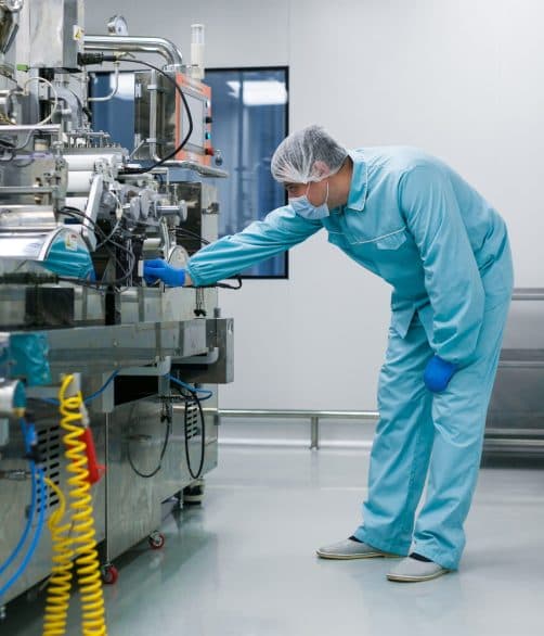 Scientist in a blue lab suit servicing a manufacturing machine